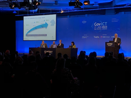 photo of four panelists and a presenter at the GovNet conference - blue blackdrop and screen with graph demonstrating rise in Cloud use.
