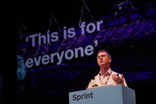 Richard Morton speaking at Sprint with a background showing “This is for everyone” in the 2012 Olympic stadium