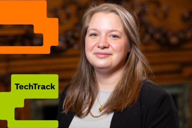A headshot of a girl wearing a black blazer, the background is brown and black, on the left of the graphic is orange and green graphic, the green has TechTrack written on it